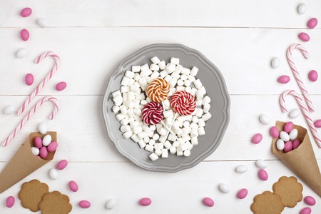 Frame colorful Candies, Striped Lollipops, cookies, Marshmallows and Lollipops on plate Top view White wooden Background Valentines Dayの写真素材