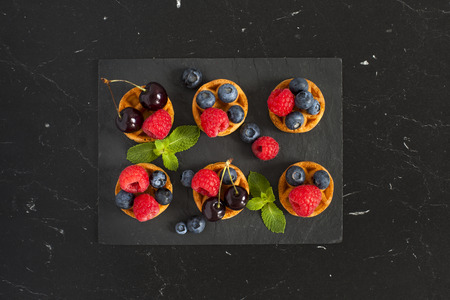 Belgian waffles with blueberries, raspberries, cherry and fresh mint on a black marble table. Top view.の写真素材