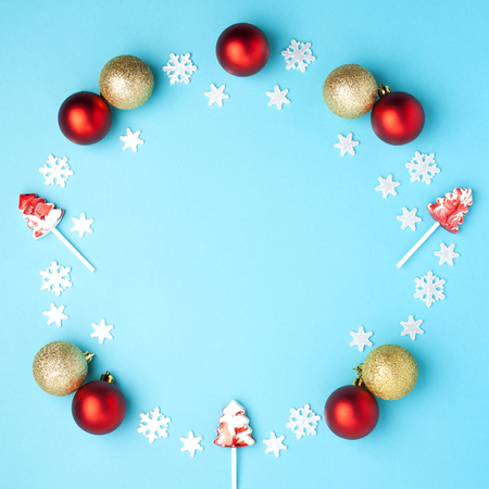 Christmas composition. Wreath made of snowflakes, red, gold balls and lollipops on pastel blue background. Christmas, winter, new year concept. Flat lay, top view, copy spaceの写真素材