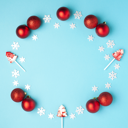 Christmas composition. Wreath made of snowflakes, red balls and lollipops on pastel blue background. Christmas, winter, new year concept. Flat lay, top view, copy spaceの写真素材