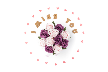 Valentine's day concept. Text I MISS YOU from cookies, frame made of paper hearts. In the center flowers in a box. Flat lay, top view, white background, isolated, copy spaceの写真素材