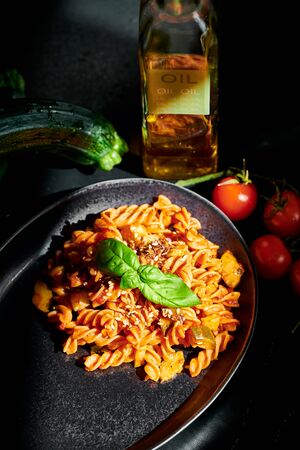Italian pasta: Chickpeas fusilli with cherry tomatoes, zucchini, linseed and olive oil, on a black background with direct sunlight on the pastaの写真素材
