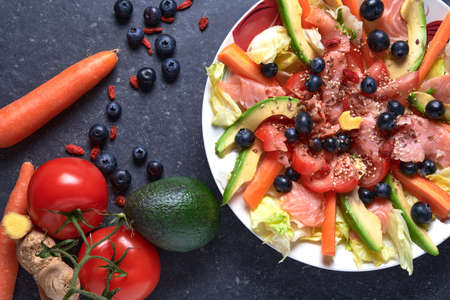 Summer salad with smoked salmon, carrots, tomatoes, avocado, ginger, blueberries, goji berries, fresh vegetables, ice salad, linseed seedsの写真素材