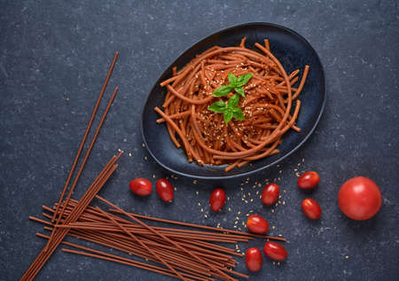 Bolognese vegan Bucatini, meatless, with soy sauce, tomatoes, sesame seeds and fresh basil, in black stone plate on dark background.の写真素材