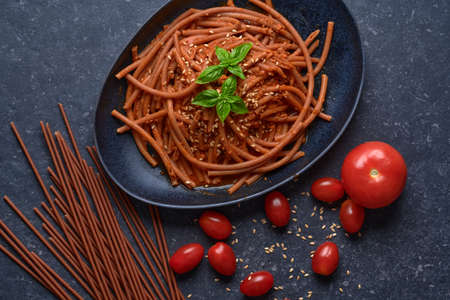 Bolognese vegan Bucatini, meatless, with soy sauce, tomatoes, sesame seeds and fresh basil, in black stone plate on dark background.の写真素材