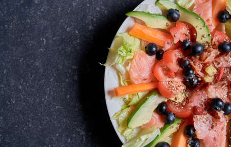 Summer salad with smoked salmon, carrots, tomatoes, avocado, ginger, blueberries, goji berries, fresh vegetables, ice salad, linseed seedsの写真素材