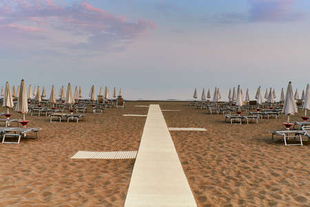 Sunbeds and umbrellas closed in the deserted beach at the end of summer season in Caorle, the small Venice.の写真素材