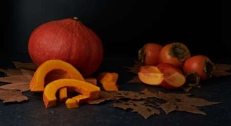 Autumnal vegetables and fruits, Pumpkin and kaki, sliced and whole, fresh and raw on a stone surface.の写真素材