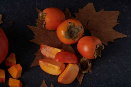 Whole and sliced Kaki with brown autumn leaves on a stone top.の写真素材
