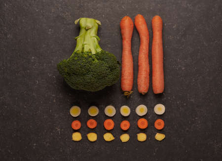 Fresh and raw broccoli and carrots, with leek and ginger cut into rounds, in a schematic composition, on a dark stone background.の写真素材