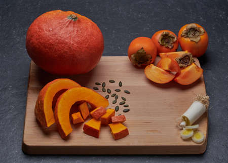 Pumpkin with its seeds, a piece of cut leek and kaki, distributed on a wooden cutting board.の写真素材