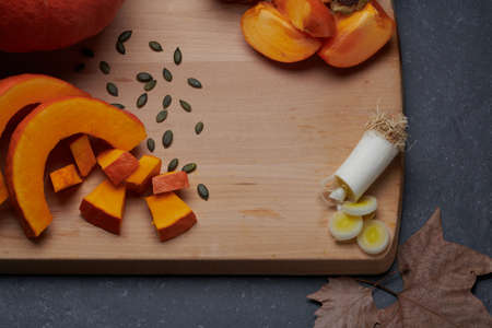 Pieces of pumpkin, leek and kaki, autumn vegetables and fruits, on a wooden cutting board.の写真素材