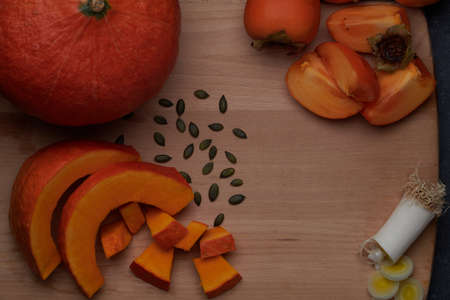 Slices of pumpkin with its seeds, a piece of cut leek and kaki, distributed on a wooden cutting board.の写真素材