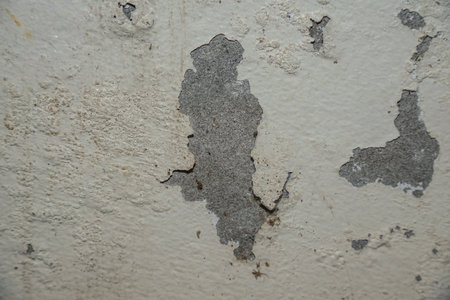 Close-up of peeling paint on a weathered wall, revealing the underlying concrete texture, showcasing age and decay.の写真素材
