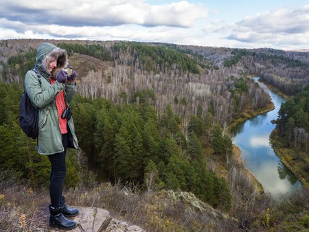 A girl on the edge of a mountain ledge photographs a beautiful turn of the river. Camp style,...