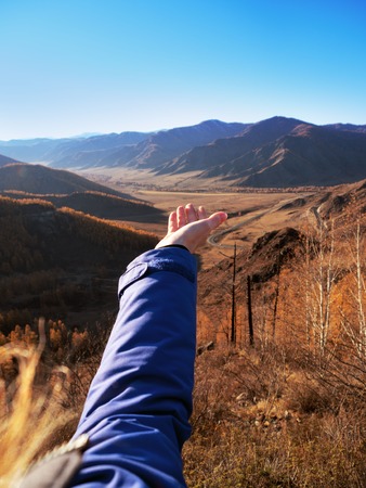 A woman's hand stretched to the beauty of the mountains. Pre-fine autumn landscape.の写真素材