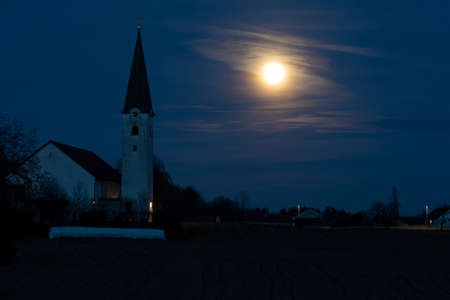 Rising full moon next to a catholic church in rural Bavaria, Germanyの写真素材