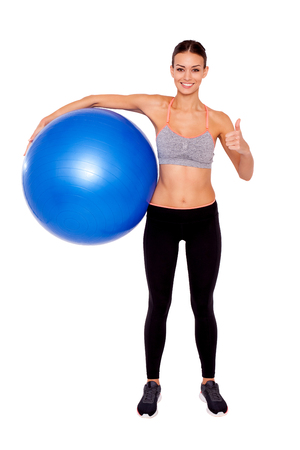 She's ready for a full body workout!  Portrait of an attractive and sporty young woman holding a pilates ball and thumb up to camera while stranding isolated.の写真素材