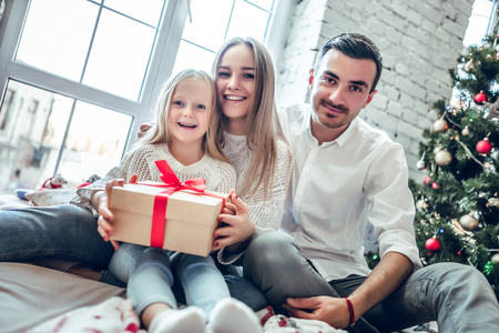 Family gather around a Christmas tree, holding a present. Happy family conceptの写真素材