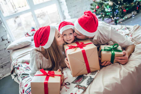 Beautiful family in Christmas interior.Happy parents kissing daughter and giving xmas present.の写真素材
