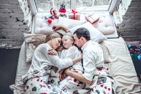 Happy family, mother, father and daughter resting on the white bed. Christmas decorationsの写真素材