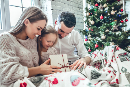 Smiling beautiful young family sitting on bed with Christmas presents in their hands.の写真素材