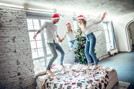 Family in red hat celebrating party are happy together. Positive emotions. Happy little girl with parents jumping on bed.の写真素材