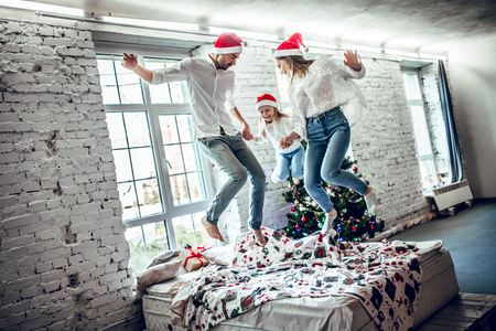 Family spending X-mas time at home. Happy family jumping on bed together.の写真素材