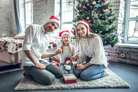Family celebrating at home. Father, mother and children on the background of the Christmas tree with presents sit on the carpet. New Year and xmas people.の写真素材