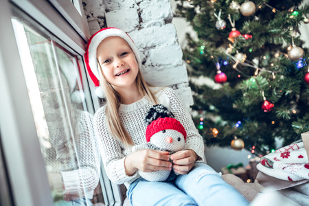 A child in the new year looks out the window. Children are waiting for Santa Claus. A child in Santa hat sits at the window.の写真素材
