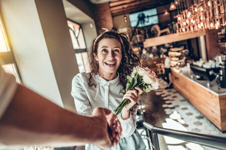 Portrait of beautiful emotional woman with bouquet flowers. Her husband holding hand when they climb the stairs of the restaurant.の写真素材