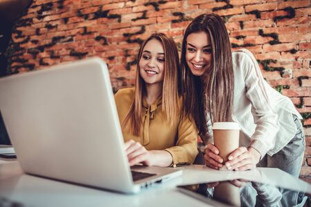 Two young women working together at startup office planning new business on brick wall background