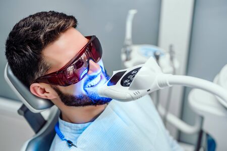 Dentist starting teeth whitening procedure with young man.の写真素材