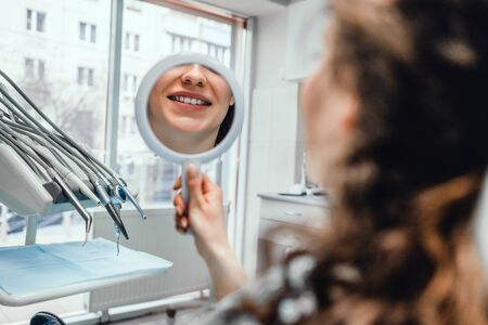 Beautiful young woman looking at mirror with smile in dentist s office.の写真素材