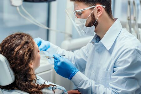 Dentist very carefully check up and repair tooth of his young female patient. Side view.の写真素材