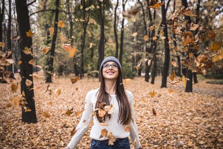 It's so fun!Young girl throwing leaves in the autumnal park.