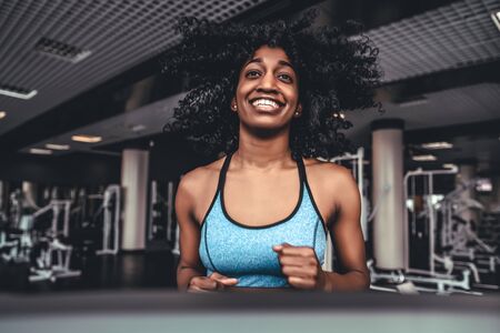 young afro woman with curly hair exercise fitness and workout while run on track in sport club. Sexy sporty girl on treadmillの写真素材