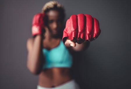 Fighter woman fist close up hit camera. Straight focus on the red glove with the rest of the image on blur. Concept about sport and people. Gray backgroundの写真素材