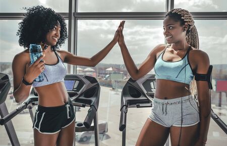 Relax after succeful trainig. Side view of two cheerful athletic afro girls in pilates healthclub. High five in gymの写真素材