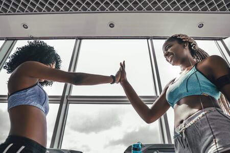 Two black athlete woman giving high five in the gym. Side view of attractive sportive afro girls on workout. Weightloss conceptの写真素材