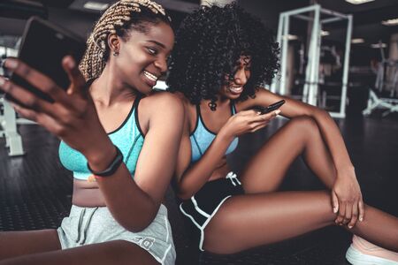 Two smiling beautiful black girls in the gym with smartphone. Sports, fitness, boxing, gym.の写真素材