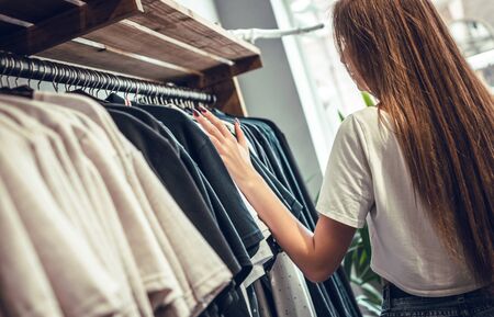 The rear view of an attractive young woman standing next to hangers, and looks at beautiful clothes...