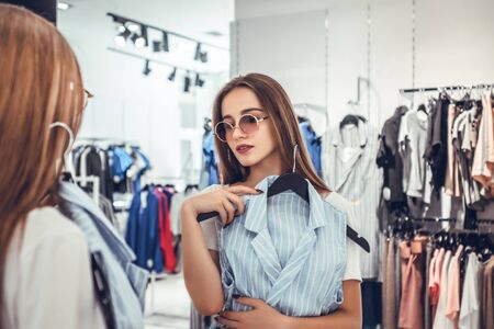 Time for shopping.Happy woman choosing clothes and looking to mirror in clothing store.の写真素材