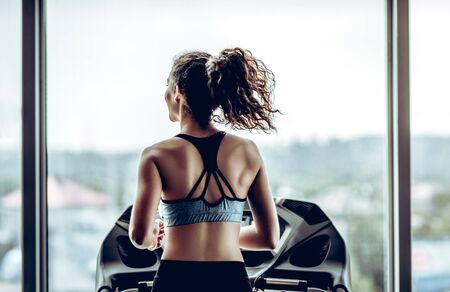 Attractive woman running on treadmill in sport gym, sport life and sport equipment. Back view.の写真素材