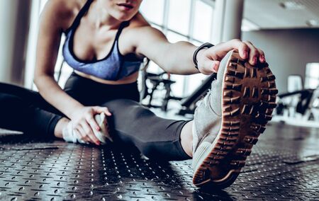 Image of gorgeous young fitness woman sitting in gym near window while make stretching exercises.の写真素材