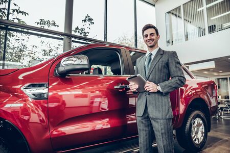 Salesman with tablet in salon on red car backgroundの写真素材