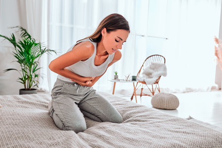 Woman having a painful stomach ache and sitting on bed with hands on abdomen. Copy spaceの写真素材