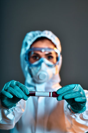 Woman in a biological protection suit holds a test tube for coronavirus in her hands. Selective focus. Vertical photoの写真素材