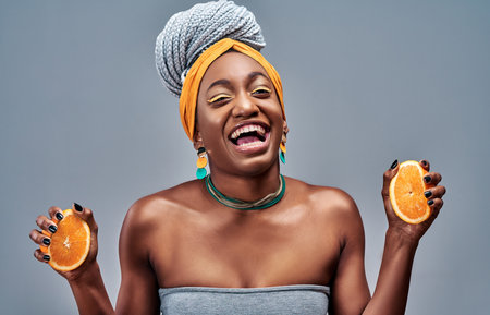 Happy comic afro american girl with beaming smile holding halves of orange in hand. Isolated on gray backgroundの写真素材