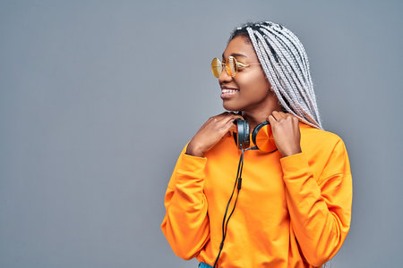 African American woman in yellow sunglasses listening to music in headphones on gray background. Copy space. Side viewの写真素材